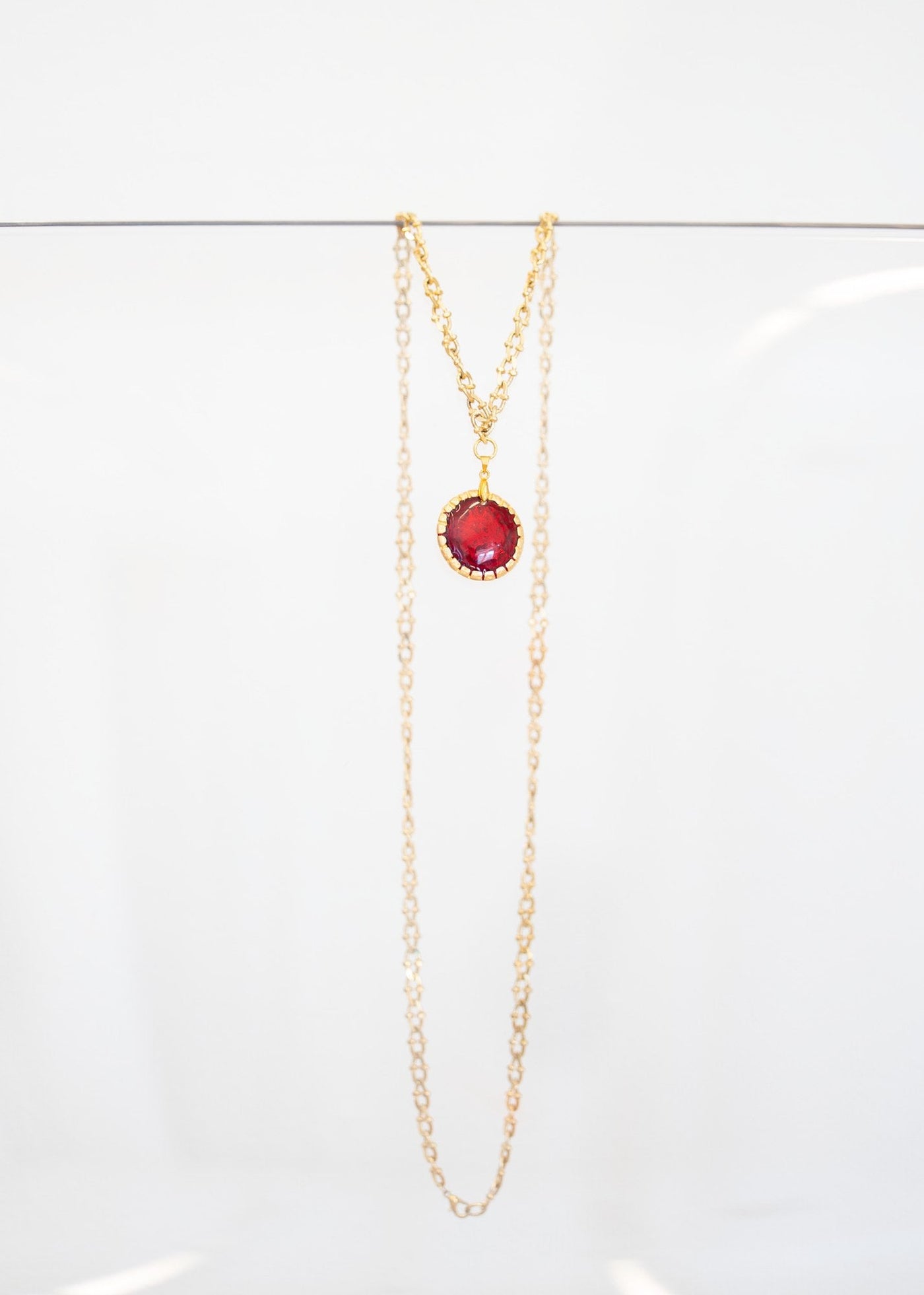 Collier « Grenat » — pendentif rond en émail rouge grenat serti d'une monture dorée festonnée, sur sautoir plaqué or à maillons ciselés. Joyeux Joyaux par Alexandra Lambert.