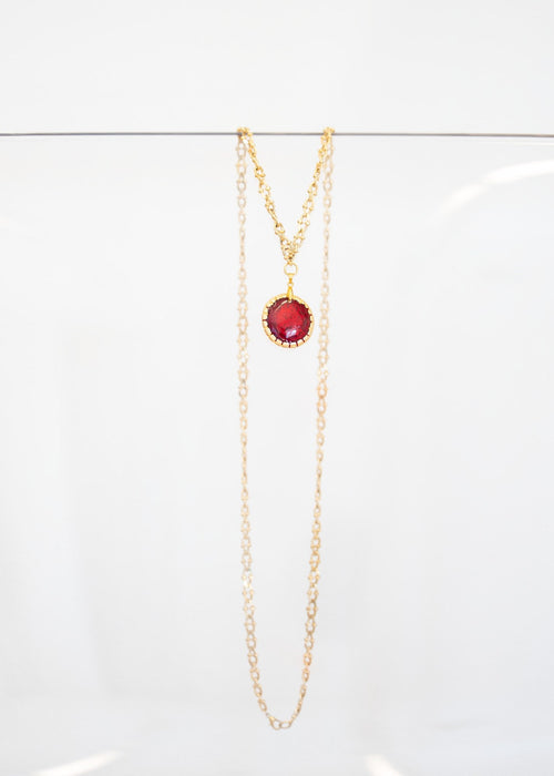 Collier « Grenat » — pendentif rond en émail rouge grenat serti d'une monture dorée festonnée, sur sautoir plaqué or à maillons ciselés. Joyeux Joyaux par Alexandra Lambert.