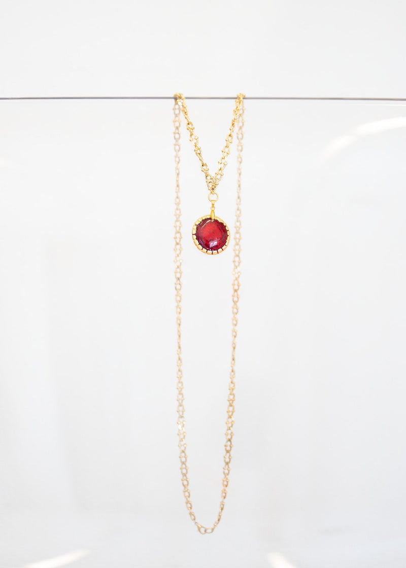 Collier « Grenat » — pendentif rond en émail rouge grenat serti d'une monture dorée festonnée, sur sautoir plaqué or à maillons ciselés. Joyeux Joyaux par Alexandra Lambert.