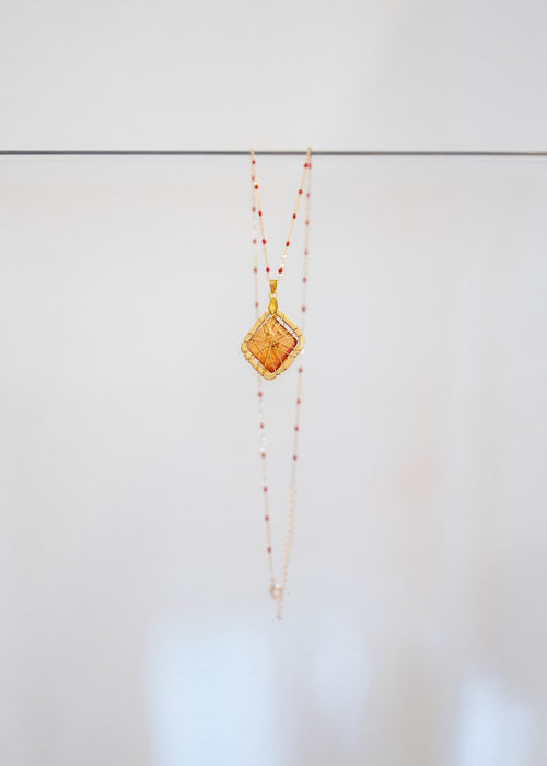 Collier « Ambre » — pendentif losange en pierre ambrée translucide dans une cage de fils dorés, sur chaîne fantaisie à perles d'émail rouge. Joyeux Joyaux par Alexandra Lambert.