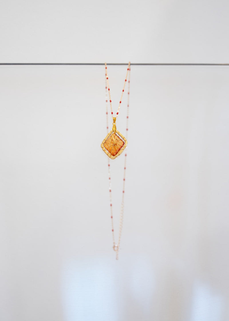 Collier « Ambre » — pendentif losange en pierre ambrée translucide dans une cage de fils dorés, sur chaîne fantaisie à perles d'émail rouge. Joyeux Joyaux par Alexandra Lambert.