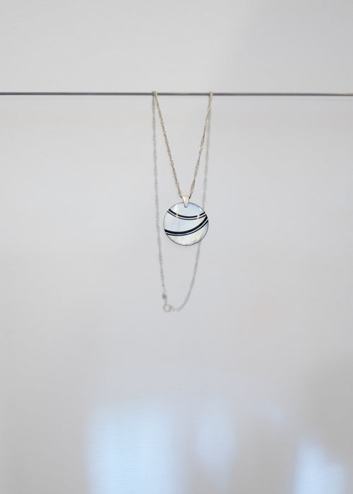 Collier « Onde » — pendentif rond en nacre blanche traversé de deux courbes noires, sur chaîne en argent torsadée. Joyeux Joyaux par Alexandra Lambert.