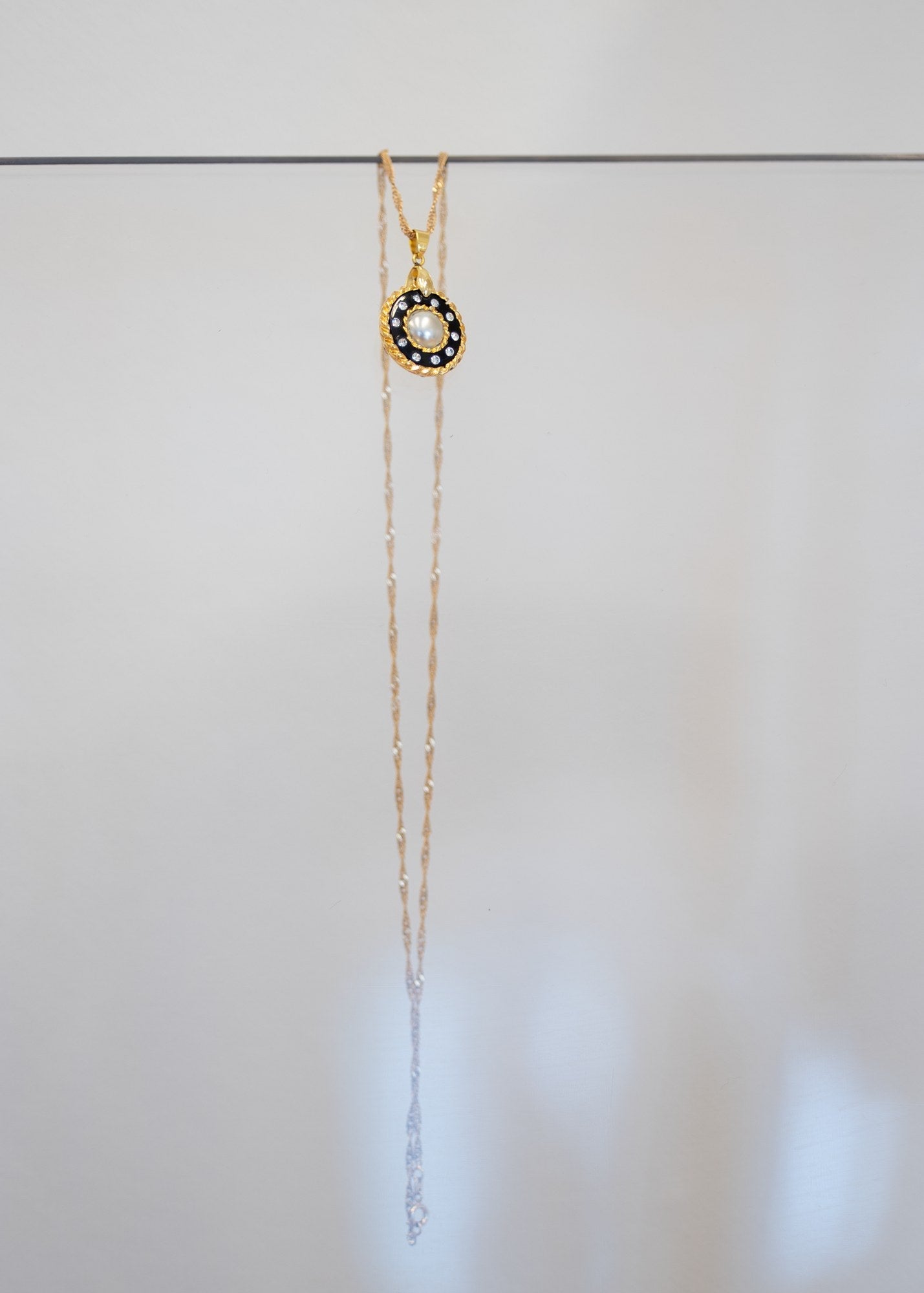 Collier « Perle Noire » — pendentif rond à perle blanche centrale entourée de cristaux sur émail noir et cerclage doré torsadé. Joyeux Joyaux par Alexandra Lambert.