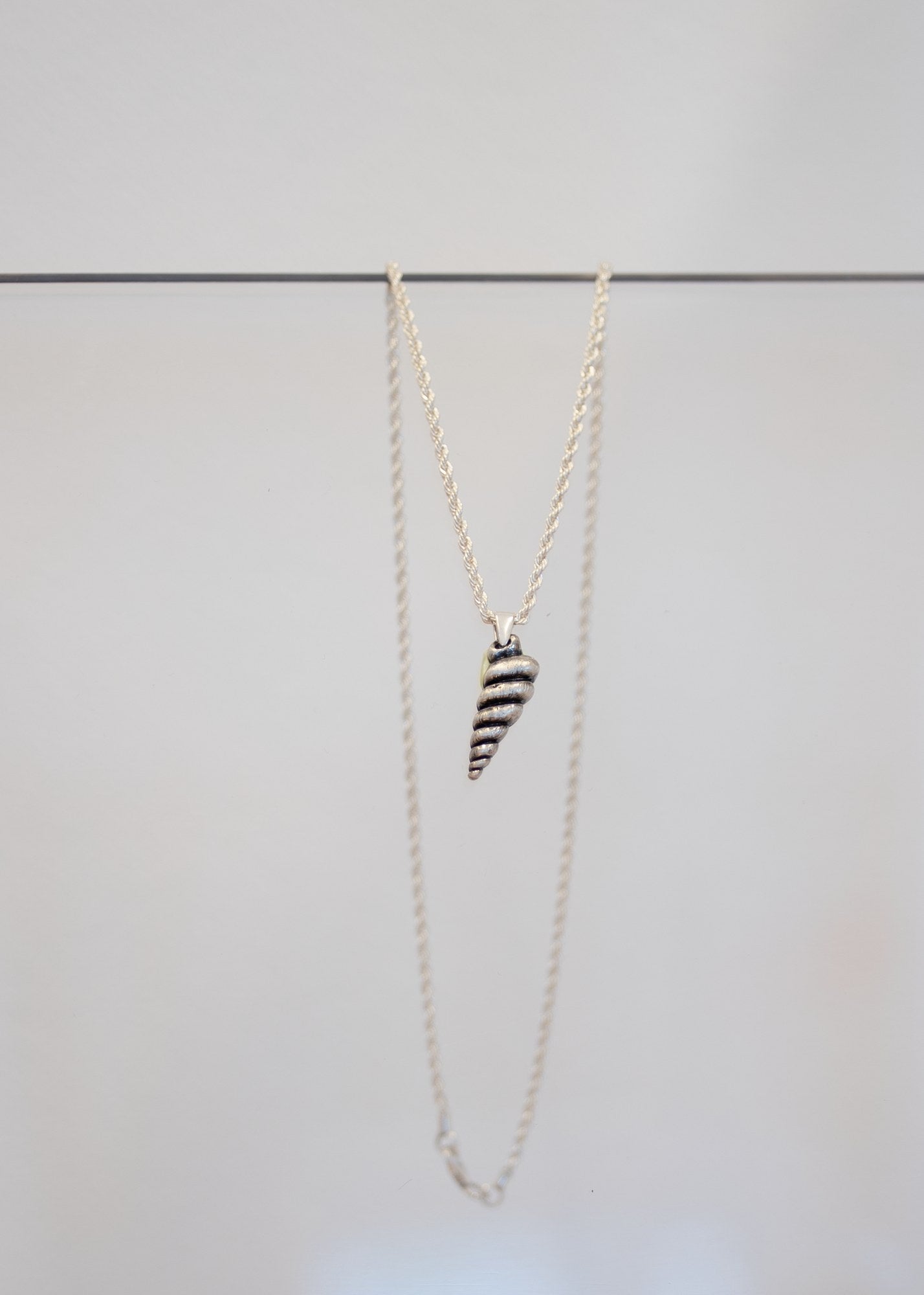 Collier « Conque » — pendentif coquillage en spirale, métal argenté patiné à cannelures, sur chaîne corde en argent. Joyeux Joyaux par Alexandra Lambert.