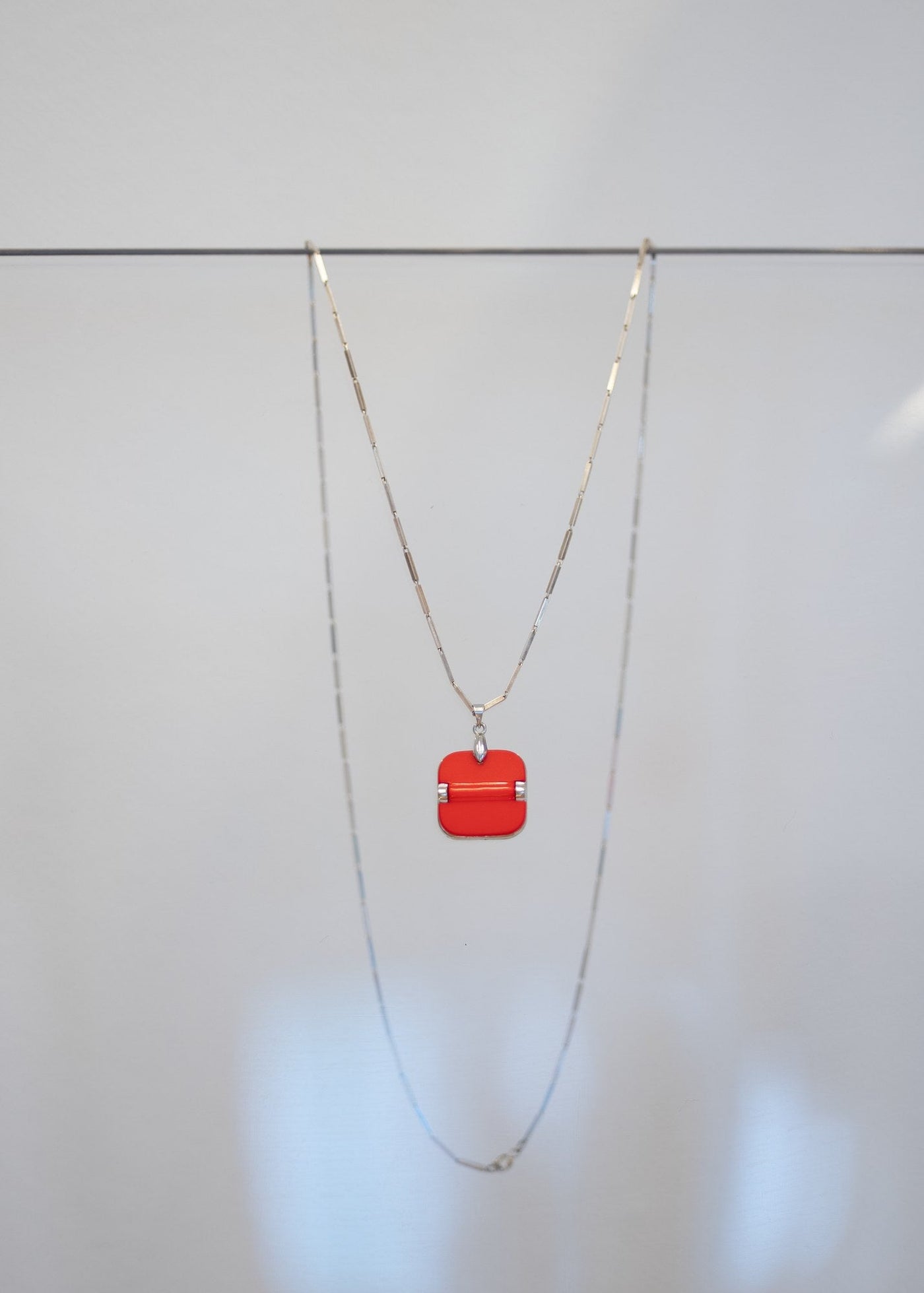 Collier « Corail » — pendentif carré en laque corail orangé traversé d'une barre cylindrique à attaches argentées, sur sautoir en argent à maillons bâtons. Joyeux Joyaux par Alexandra Lambert.